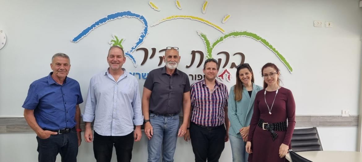 ראש המועצה, מנכל המשרד לשיתוף פעולה אזורית , אנשי משרדו ומנהל אגף הישובים עומדים ליד הקיר עם הלוגו 